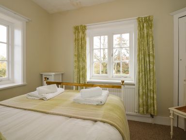 A bedroom with a bed with folded towels on it and windows with green patterned curtains at Beckhythe Cottage in Overstrand