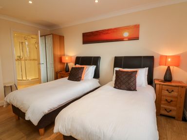 A bedroom with two single beds a wooden wardrobe bedside tables and lamps at Beach Lodge in Woolacombe