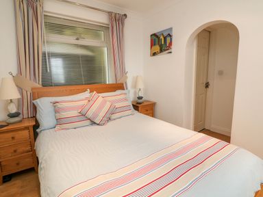 A bedroom with a bed with striped pillows and bed runner wooden bedside tables with lamps and a window with blinds and striped curtains at Beach Lodge in Woolacombe