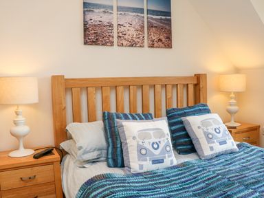 A bedroom with a wooden bed frame blue pillows and blankets bedside tables with lamps and a triptych beach photo above the bed at Beach Lodge in Woolacombe