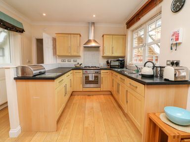 A kitchen with wooden cabinets a stove and oven a kettle toaster bread box and a blue bowl at Beach Lodge in Woolacombe