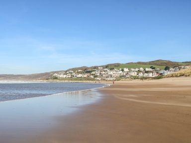 A sandy beach with water on the left and houses on hills in the background at Beach Lodge in Woolacombe