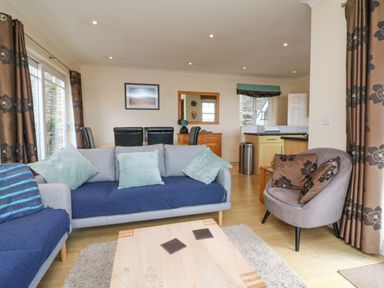 A living room with sofas a round chair a wooden coffee table and dining chairs at Beach Lodge in Woolacombe