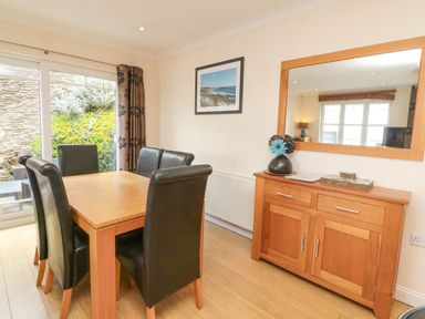A dining room with wooden table black chairs wooden sideboard with mirror and sliding glass door at Beach Lodge in Woolacombe