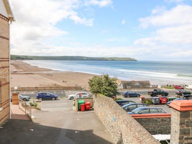 View of a beach with parked cars and a road in the foreground and hills in the background at Beach Lodge in Woolacombe