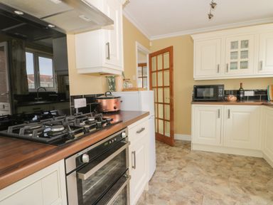 A kitchen with white cabinets a stove oven microwave countertop appliances and a wooden door at Arbour Retreat in Filey