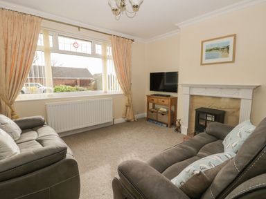 A living room with two sofas a TV on a wooden stand a fireplace and a large window with curtains at Arbour Retreat in Filey
