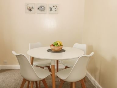 A round white dining table with four white chairs and a bowl of fruit on top with fish artwork on the wall at Arbour Retreat in Filey