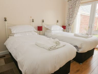 A bedroom with two single beds with white linens and towels by a window with floral curtains at Arbour Retreat in Filey