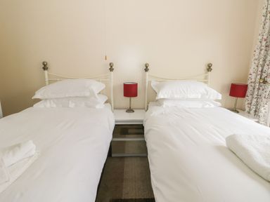 A bedroom with two single beds with white bedding and red lamps on bedside tables at Arbour Retreat in Filey