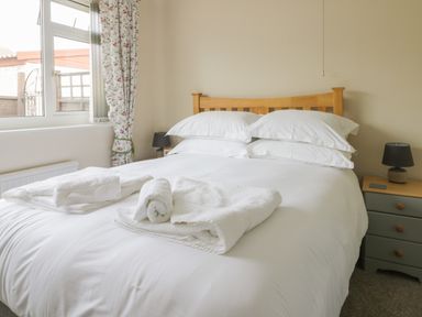A bedroom with a wooden bed frame white bedding side tables and folded towels on the bed at Arbour Retreat in Filey