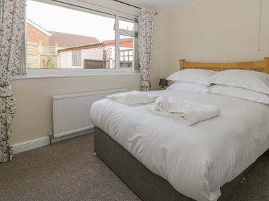 A bedroom with a double bed and folded towels on the bed near a window with floral curtains at Arbour Retreat in Filey