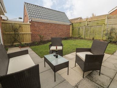 A patio with outdoor wicker furniture including a sofa and two chairs around a glass table with two glasses and a bottle of wine at Arbour Retreat in Filey
