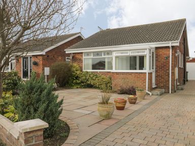 A brick bungalow with a tiled roof and a paved driveway with potted plants and bushes at Arbour Retreat in Filey