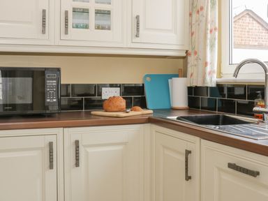 A kitchen counter with a microwave loaf of bread cutting board paper towel holder sink and faucet at Arbour Retreat in Filey