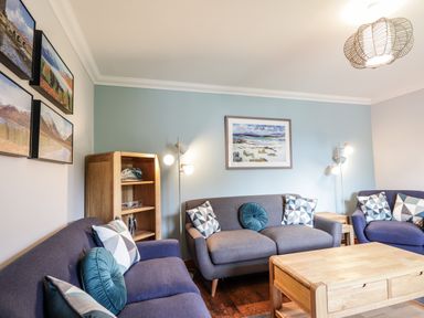 A living room with three blue sofas a wooden coffee table a wooden shelf lamps and landscape paintings at Silver Birch Lodge in Ratagan Glenshiel near Dornie