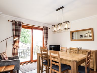 A dining room with a wooden table and chairs a sideboard a mirror and a large window with plaid curtains at Silver Birch Lodge in Ratagan Glenshiel near Dornie