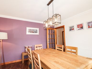 A dining room with a wooden table and chairs a purple accent wall with artwork a floor lamp and hanging light fixtures at Silver Birch Lodge in Ratagan Glenshiel near Dornie