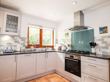 A kitchen with white cabinets a gas stove oven a window and countertop appliances at Silver Birch Lodge in Ratagan Glenshiel near Dornie