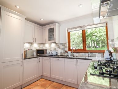 A kitchen with white cabinets a gas stove microwave toaster and sink below a window at Silver Birch Lodge in Ratagan Glenshiel near Dornie