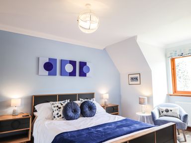 A bedroom with a bed pillows armchair side tables and artwork above the bed at Silver Birch Lodge in Ratagan Glenshiel near Dornie