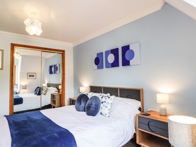 A bedroom with a bed featuring blue and white pillows and a blanket beside two wooden nightstands with lamps and a mirrored wardrobe at Silver Birch Lodge in Ratagan Glenshiel near Dornie
