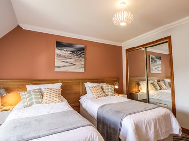 A bedroom with two single beds white linens pillows bedside lamps a painting and mirrored wardrobe at Silver Birch Lodge in Ratagan Glenshiel near Dornie