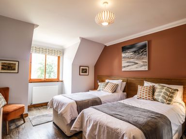 A bedroom with two single beds a window and an armchair at Silver Birch Lodge in Ratagan Glenshiel near Dornie