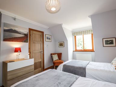 A bedroom with two single beds gray blankets wooden door and a window with patterned blind at Silver Birch Lodge in Ratagan Glenshiel near Dornie