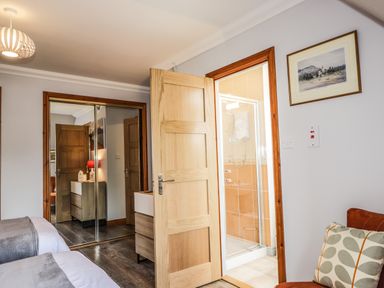 A bedroom with twin beds a dresser and a bathroom with a shower at Silver Birch Lodge in Ratagan Glenshiel near Dornie