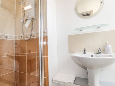 A bathroom with a shower area, a white sink, a round mirror, and a bottle on the sink at Silver Birch Lodge in Ratagan Glenshiel near Dornie