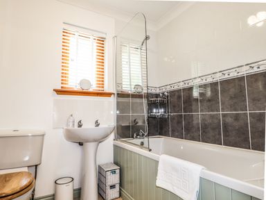 A bathroom with a toilet a sink a bathtub with shower and a window with blinds at Silver Birch Lodge in Ratagan Glenshiel near Dornie