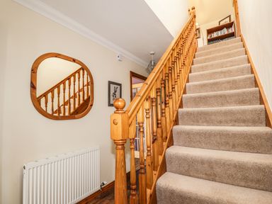 A carpeted staircase with wooden railing and a wall mirror reflecting the banister at Silver Birch Lodge in Ratagan Glenshiel near Dornie