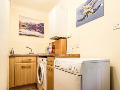A utility room with a washing machine, dryer, sink and cupboard at Silver Birch Lodge in Ratagan Glenshiel near Dornie