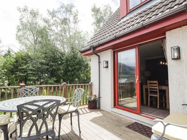 A balcony with a metal table and chairs with cushions outside a house with sliding glass doors at Silver Birch Lodge in Ratagan Glenshiel near Dornie
