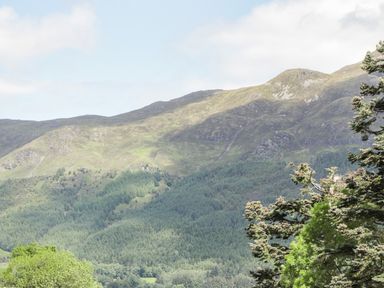 A mountain landscape with a forested area in the foreground and a partly cloudy sky at Silver Birch Lodge in Ratagan Glenshiel near Dornie