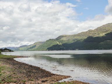 A lake with a rocky shore and hills in the background at Silver Birch Lodge in Ratagan Glenshiel near Dornie