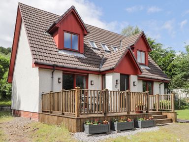 A two story house with brown tiled roof wooden deck and flower boxes in front at Silver Birch Lodge in Ratagan Glenshiel near Dornie
