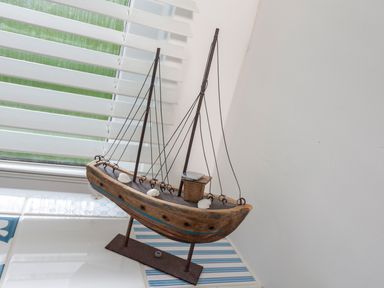 A decorative wooden model boat with strings displayed on tiles near a window with blinds at The Hut in Dartmouth
