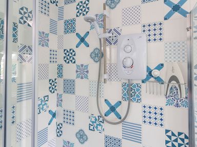 A shower area with a wall-mounted electric shower unit and patterned blue and white tiles at The Hut in Dartmouth