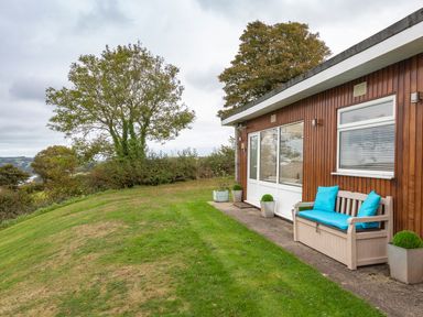 A grassy yard with a wooden bench and potted plants outside a wood-paneled house at The Hut in Dartmouth