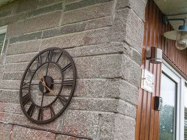 A wall clock on a stone wall next to a wooden door with a light and a sign that says 322 The Hut in Dartmouth