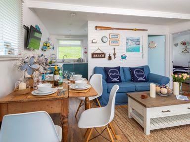 A dining and living area with a wooden table set for four and a blue sofa with cushions at The Hut in Dartmouth