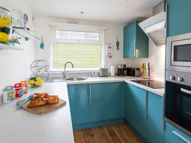 A kitchen with blue cabinets a cutting board with croissants a sink a toaster and a microwave at The Hut in Dartmouth
