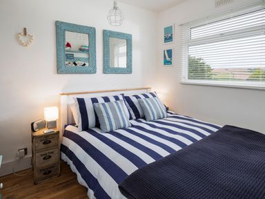 A bedroom with a double bed with striped bedding two blue framed mirrors and a window with blinds at The Hut in Dartmouth