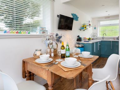 A dining area with a wooden table set with bowls and glasses next to a kitchen with blue cabinets at The Hut in Dartmouth