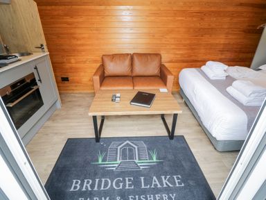 A living room with a sofa and kitchen unit at Acorn Lodge At Bridge Lake Farm & Fishery Chacombe