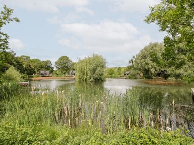 A view of a lake with trees and houses at Acorn Lodge At Bridge Lake Farm & Fishery Chacombe