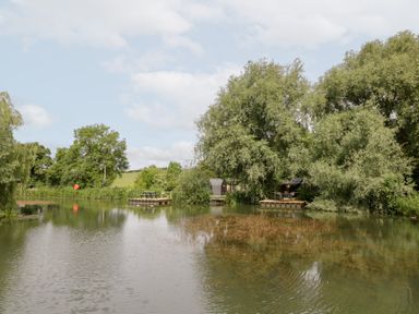 A pond with trees and dock at Acorn Lodge At Bridge Lake Farm & Fishery Chacombe