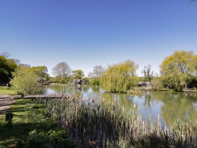 A scenic view of a lake with houses and greenery at Acorn Lodge At Bridge Lake Farm & Fishery Chacombe